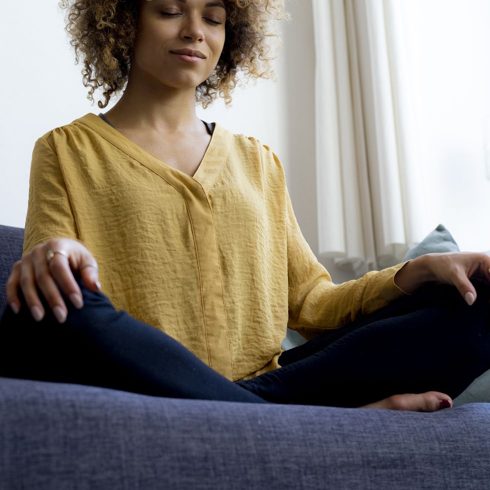 young woman sitting on couch at home meditating