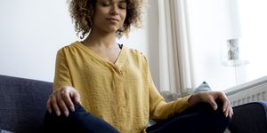 Young woman sitting on couch at home meditating