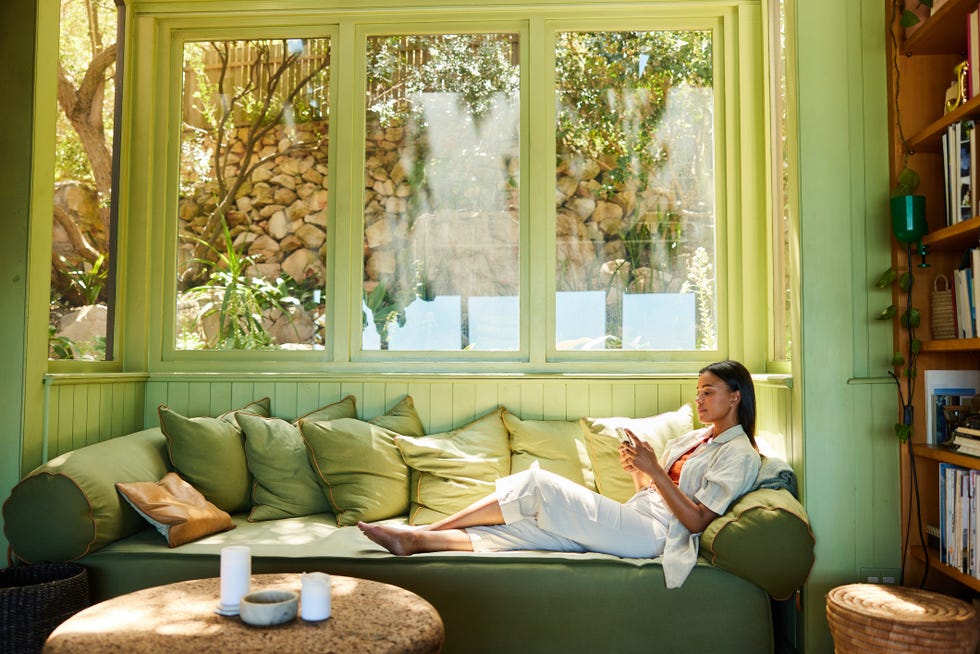 young woman sitting on her sofa and texting on her phone