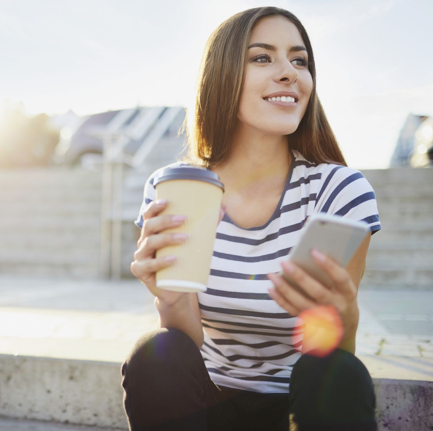 Young woman sitting on stairs in the city with phone and coffee