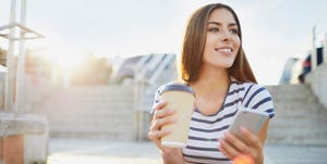 Young woman sitting on stairs in the city with phone and coffee