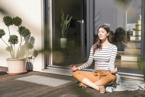 Young woman sitting on terrace at home practicing yoga