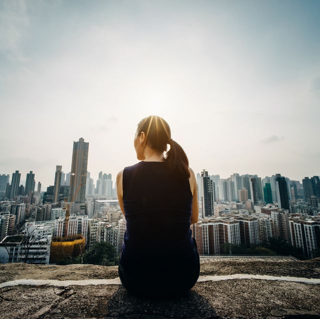 young woman sitting on the top of mountain enjoying the panoramic view of spectacular city skyline