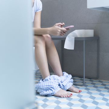 young woman sitting on toilet and using smartphone