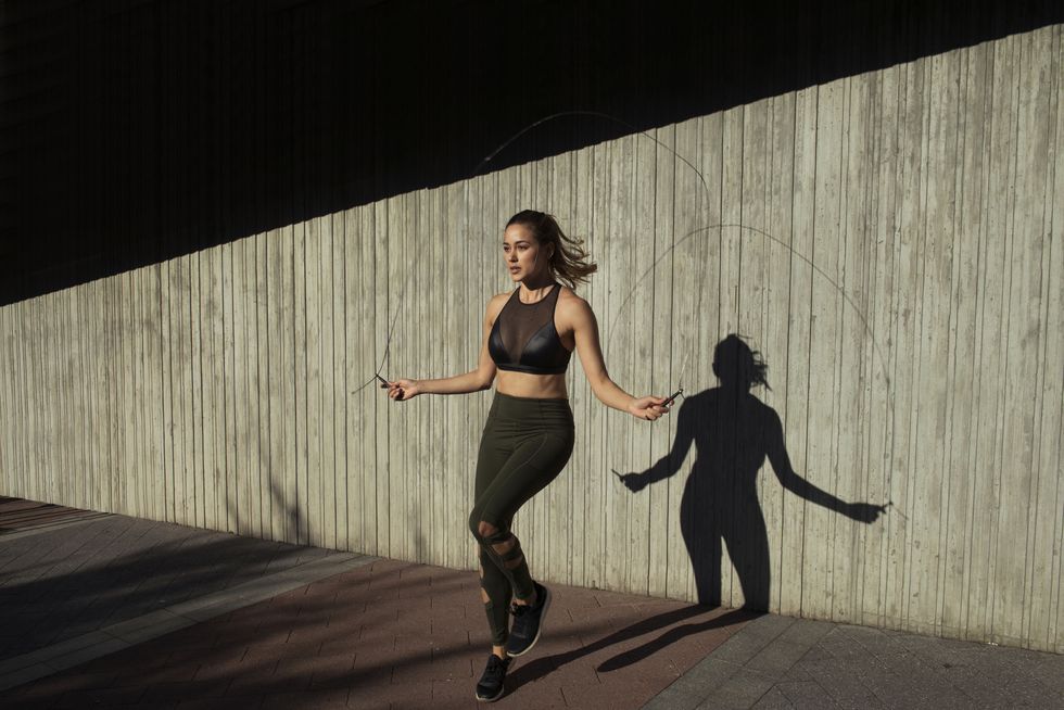 young woman skipping while exercising against wall