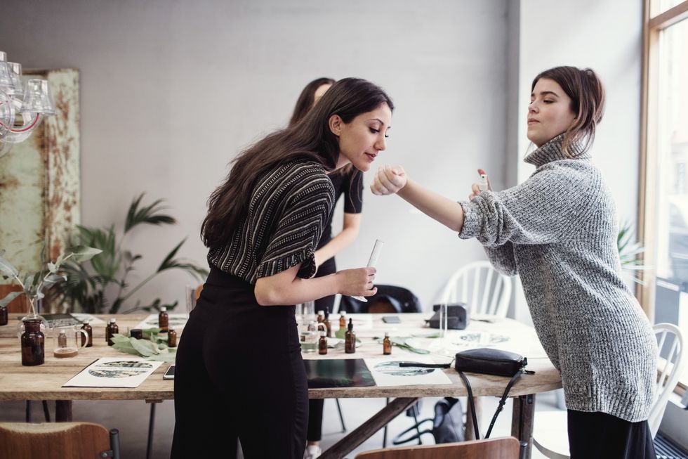 Young woman smelling perfume fragrance from female colleagues wrist while standing at workshop