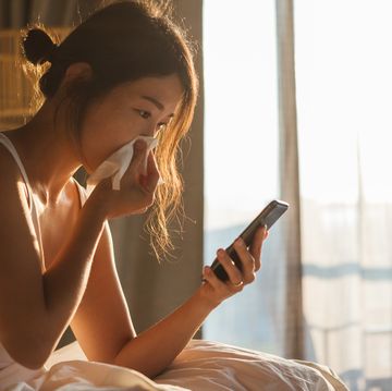 young woman sneezing while using mobile phone in bed