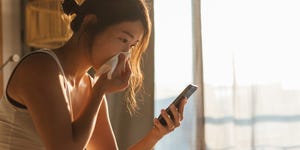 young woman sneezing while using mobile phone in bed