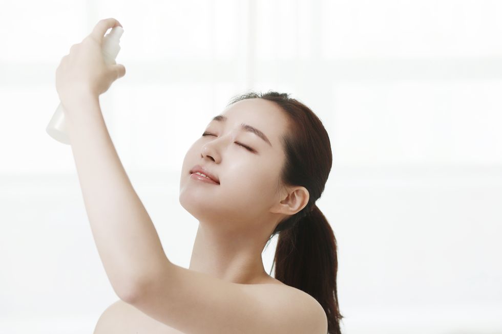 young woman spraying mist on face with eyes closed