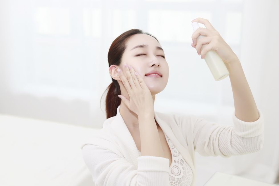 Young woman spraying mist on face with eyes closed