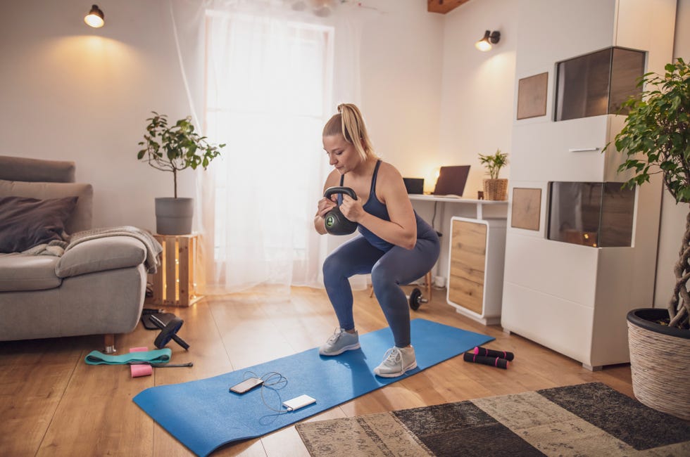 young woman squatting with kettlebell on yoga mat in living room