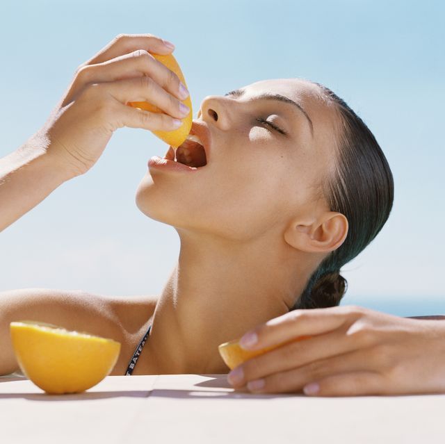 young woman squeezing juice from orange into mouth, close up
