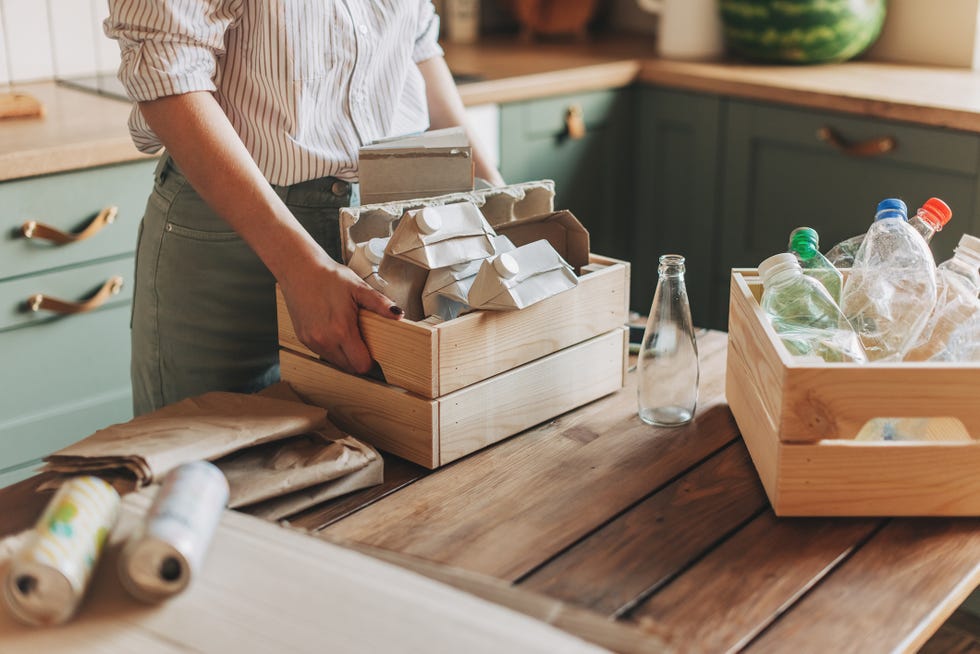 young woman standing at the table in the kitchen and segregating waste to correct containers