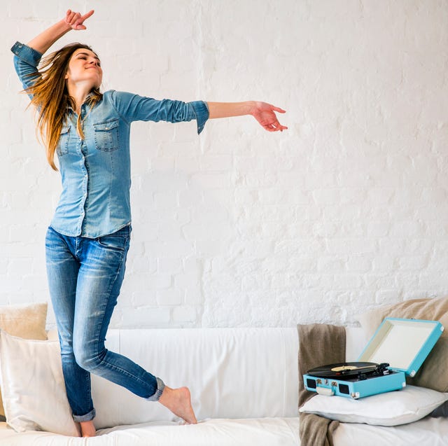 young woman standing on sofa dancing to vintage record player