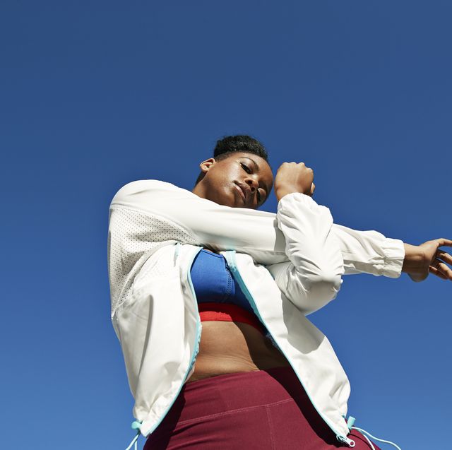 young woman stretching arm against clear blue sky on sunny day