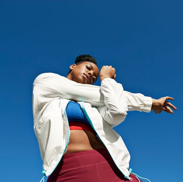 young woman stretching arm against clear blue sky on sunny day