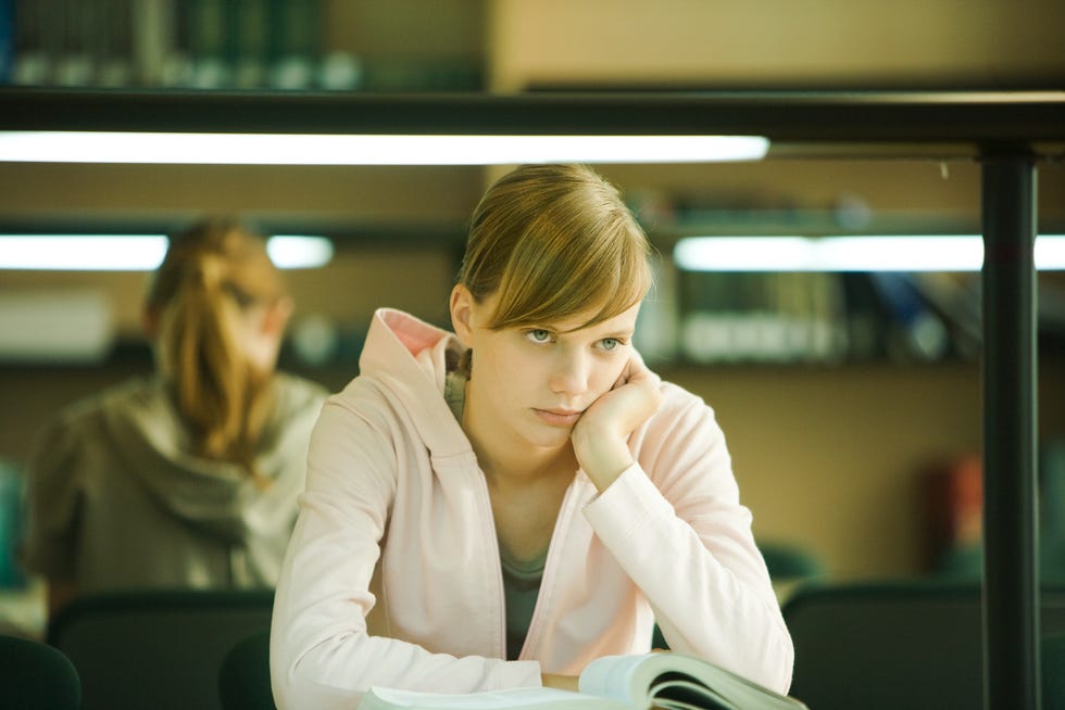 Young woman studying in university library, holding head, looking away