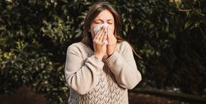 young woman suffering spring allergy and blowing nose with a tissue in the nature