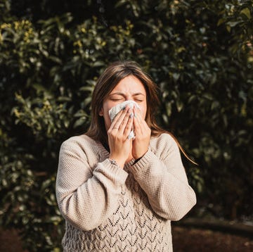 young woman suffering spring allergy and blowing nose with a tissue in the nature