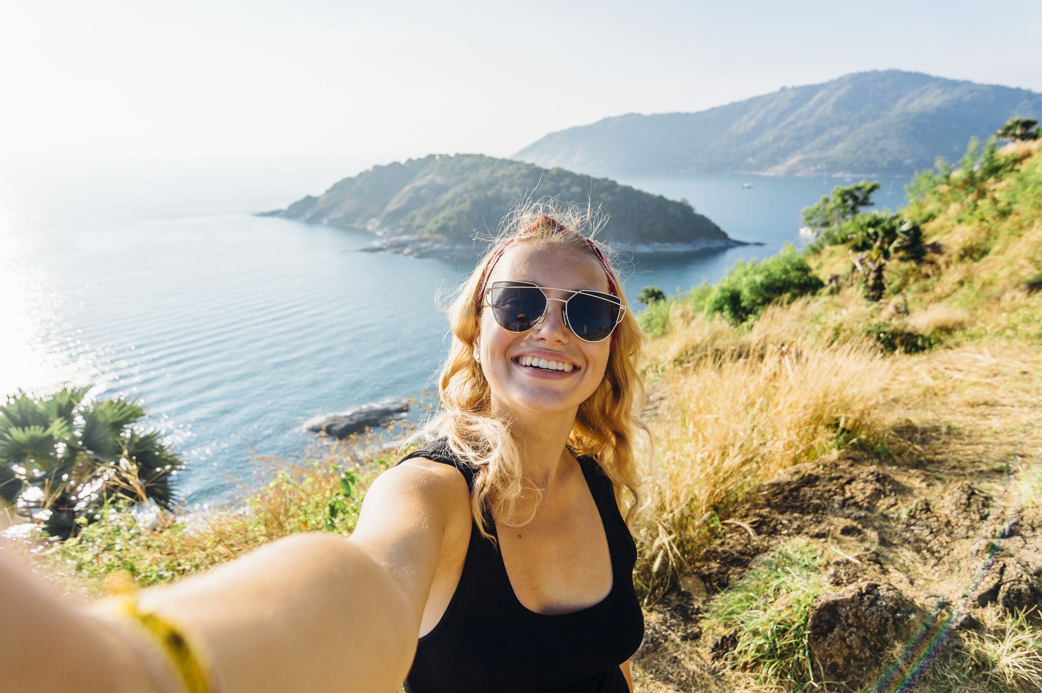 Young woman takes selfie, on hillside above sea