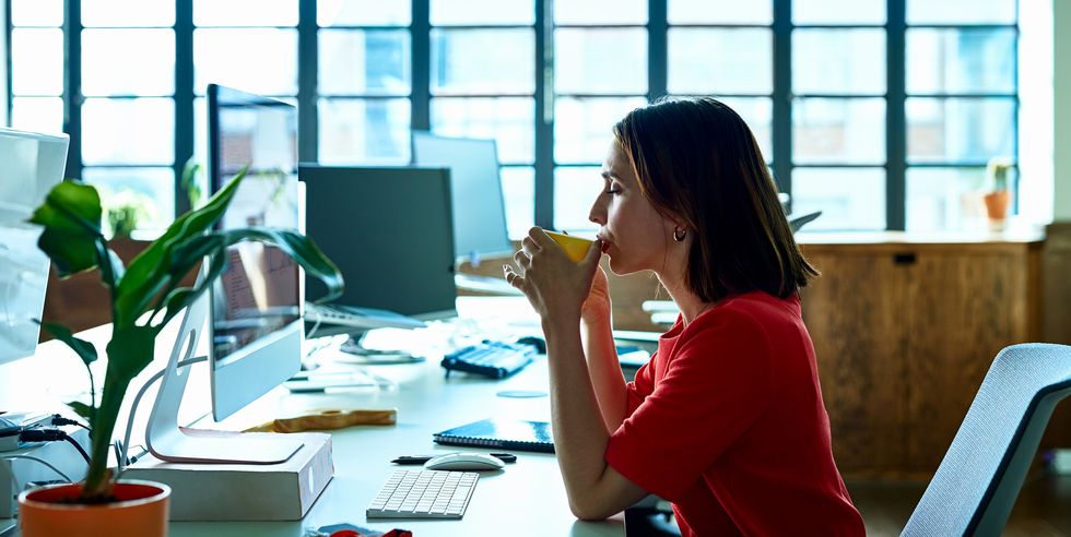 young woman taking coffee break at desk with eyes closed