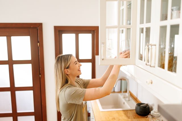 young woman taking drinking glasses from a kitchen cabinet