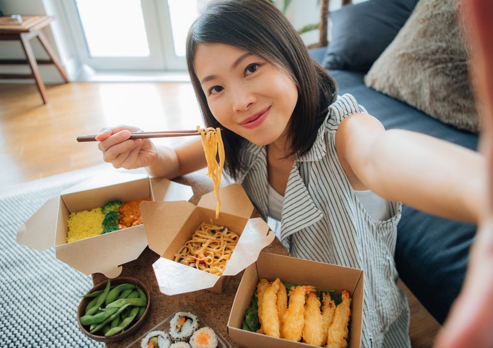 young woman taking selfie while eating takeaway food