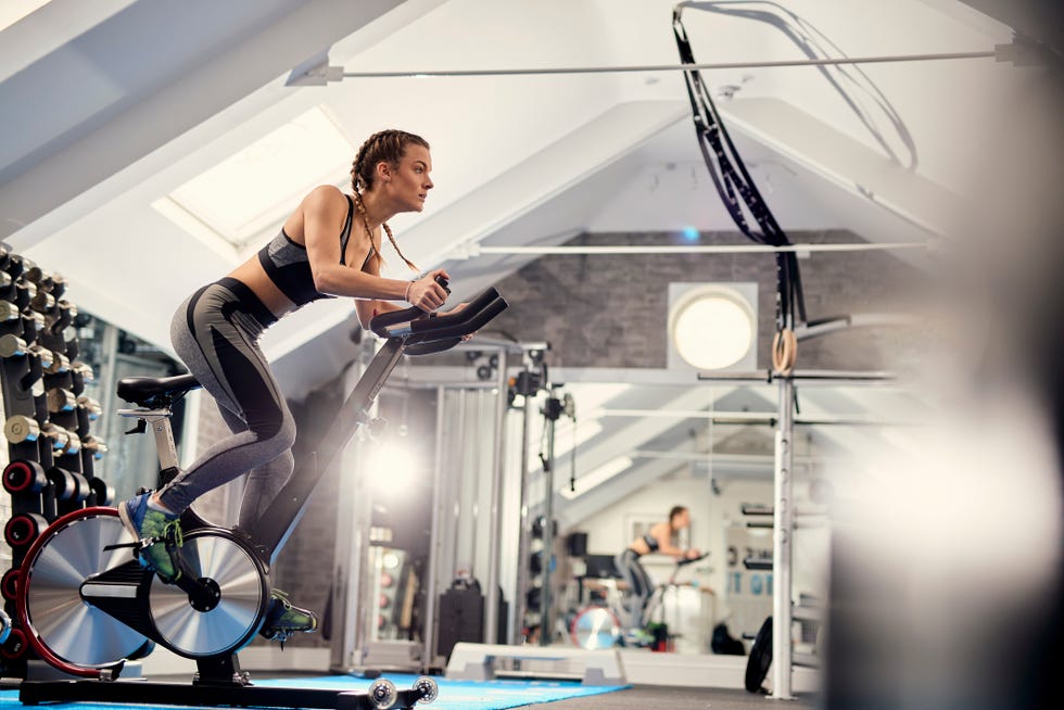 young woman training, pedalling exercise bike in gym