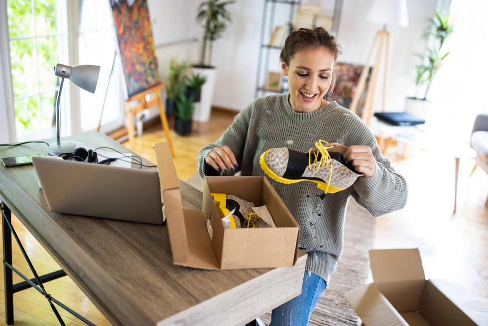 young woman unpacking boots from cardboard box that she have received after online shopping