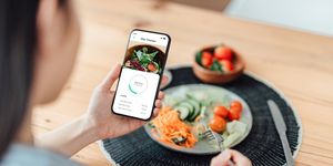 young woman using calorie counter app on smartphone while eating salad