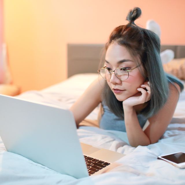 Young Woman Using Laptop While Lying On Bed At Home