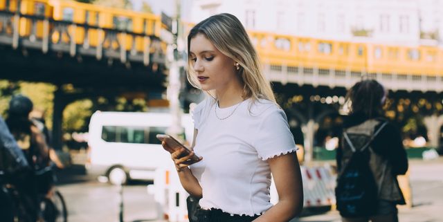 Young woman using mobile phone while walking by street in city