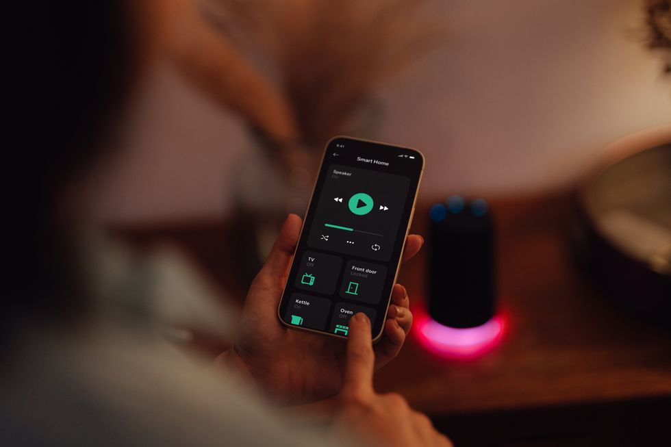 young woman using smartphone to control smart speaker of a modern smart home