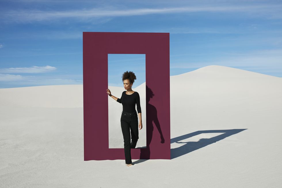 young woman walking through door frame at desert against sky