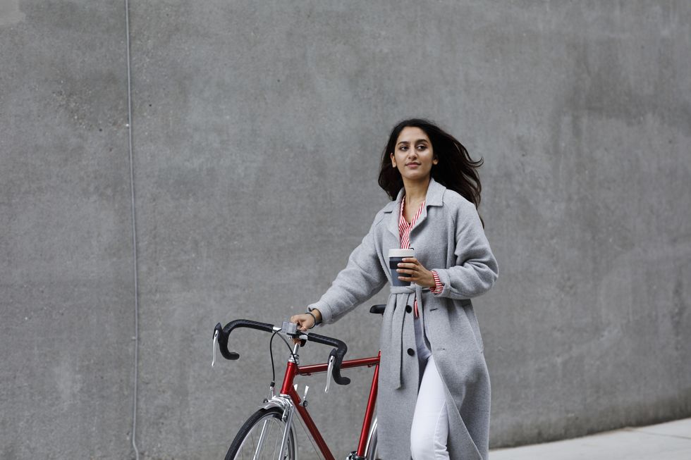 young woman walking with bicycle, with reusable coffee cup in hand