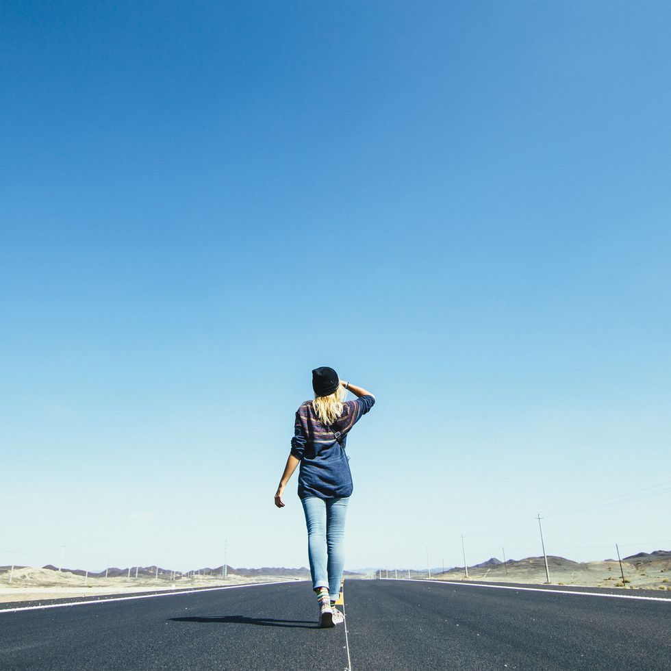 young woman walks along long rural highway