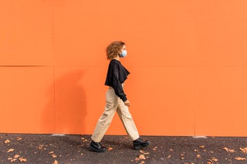 young woman wearing face mask walking against orange wall