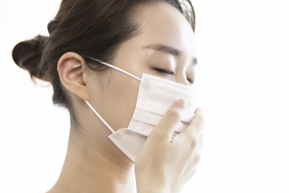 Young woman wearing protective face mask with cough