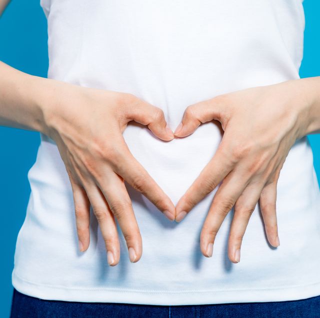young woman who makes a heart shape by hands on her stomach