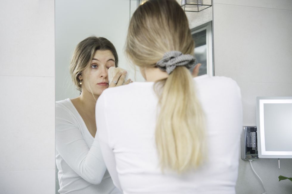 young woman wiping makeup off face in bathroom