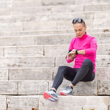 a young woman with a sporty figure looks at her heart rate and sports performance on a smart phone, sitting on the steps in the park