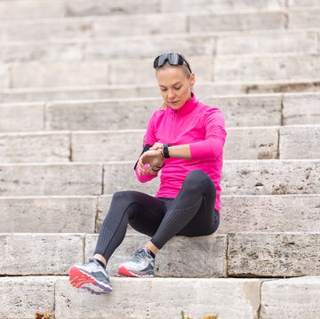 A young woman with a sporty figure looks at her heart rate and sports performance on a smart phone, sitting on the steps in the park. a young woman with a sporty figure looks at her heart rate and sports performance on a smart phone, sitting on the steps in the park