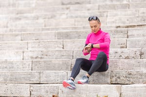 a young woman with a sporty figure looks at her heart rate and sports performance on a smart phone, sitting on the steps in the park