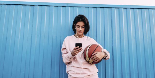 Young woman with basketball, smartphone and earphones at container
