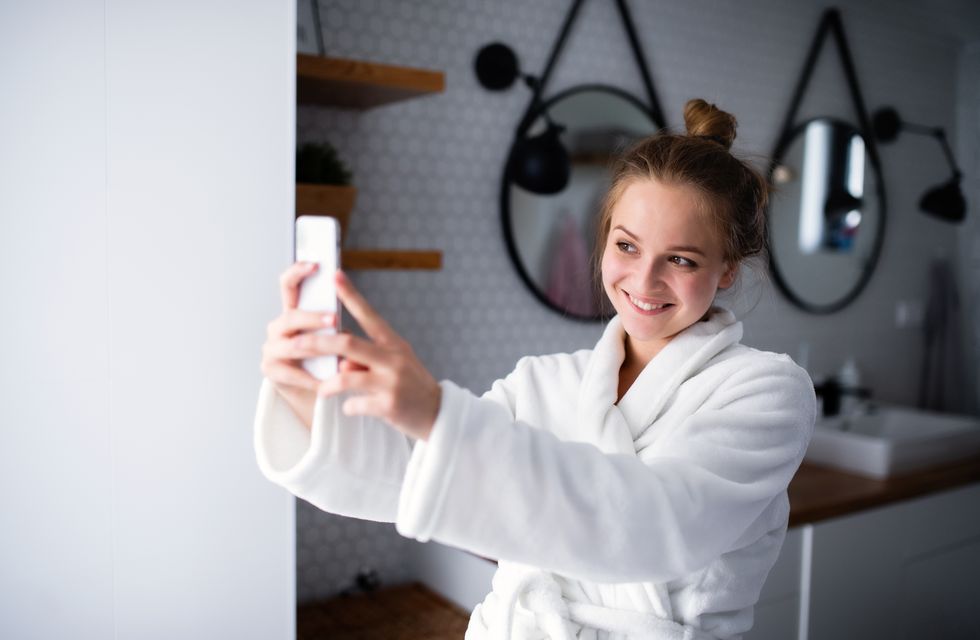 young woman with bathrobe and smartphone in bathroom, taking selfie