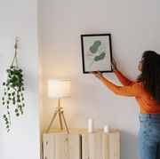 young woman with curly hair hanging picture frame on wall at home