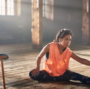 Young woman with earbuds stretching in gym.