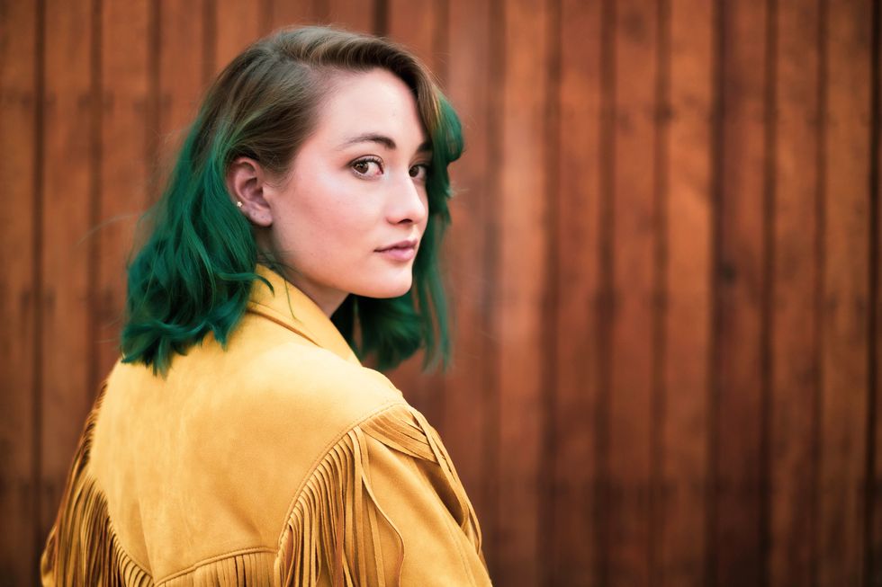 young woman with green hair looking at the camera in mexico city against a wooden background