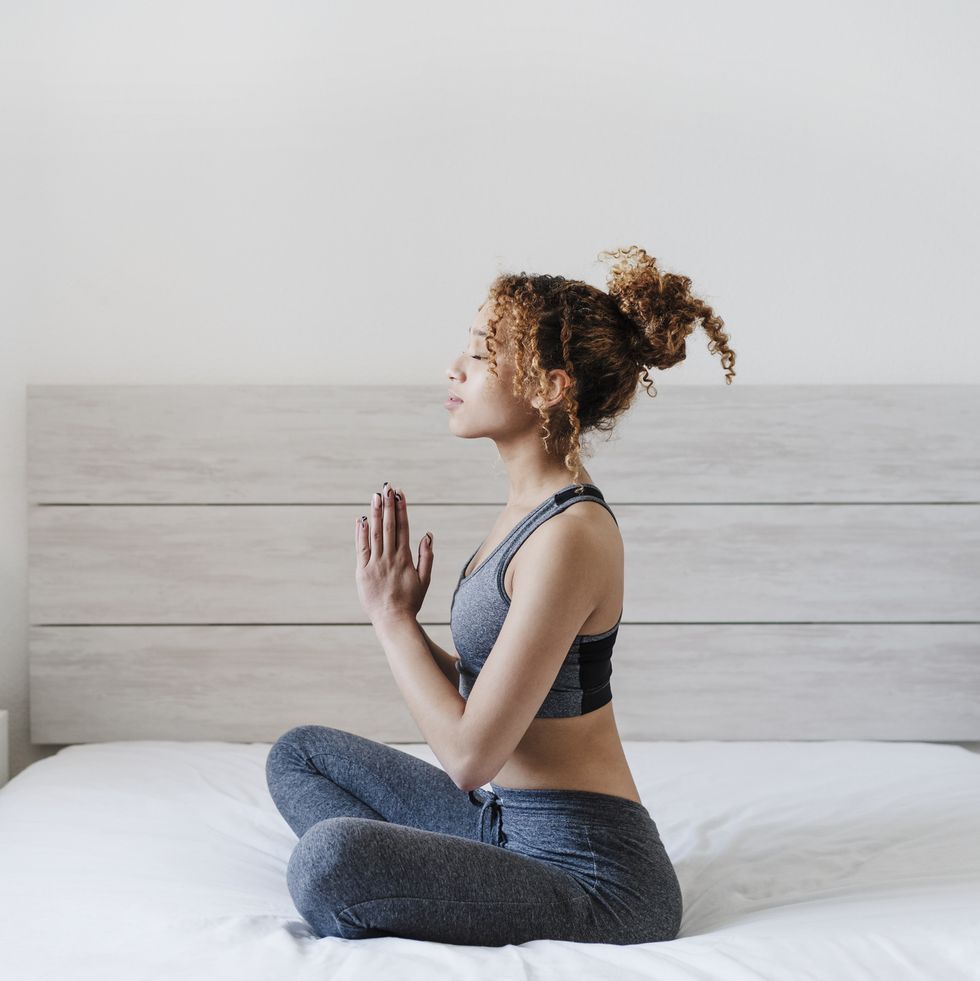 young woman with hands clasped meditating on bed at home