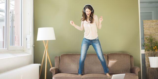 Young woman with headphones standing on couch screaming and dancing